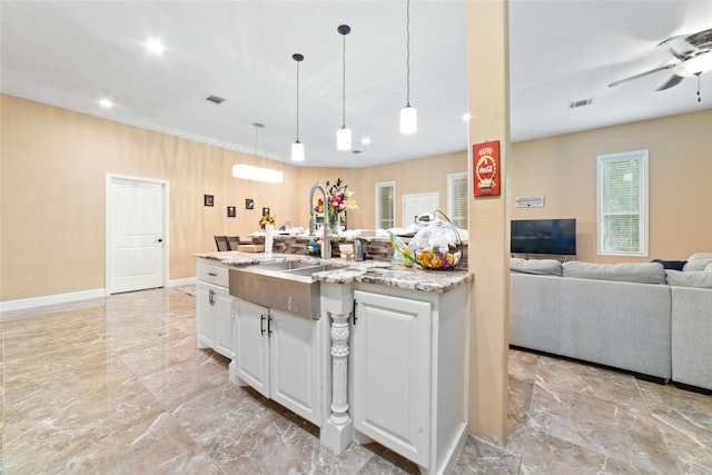 kitchen with white cabinetry, sink, ceiling fan, an island with sink, and decorative light fixtures