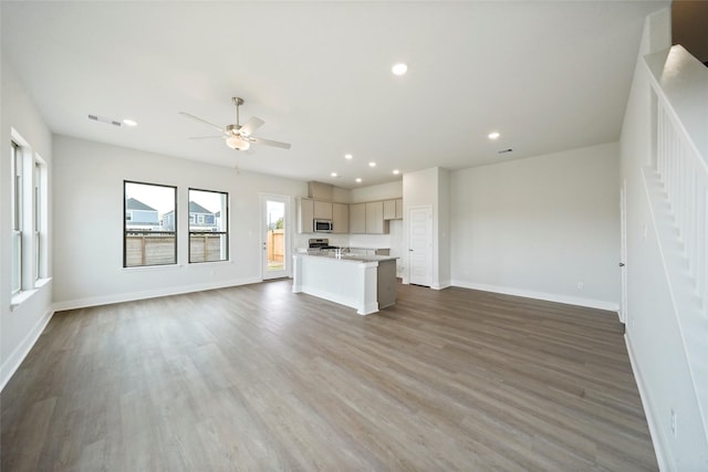 kitchen with appliances with stainless steel finishes, a breakfast bar, ceiling fan, wood-type flooring, and a center island with sink