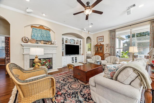 living room featuring ceiling fan, dark wood-type flooring, a premium fireplace, built in features, and crown molding