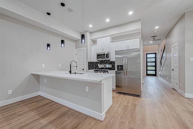 kitchen featuring stainless steel appliances, kitchen peninsula, decorative light fixtures, white cabinets, and light wood-type flooring