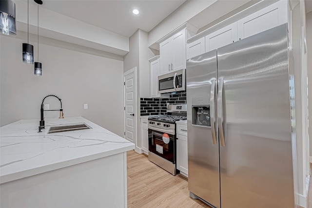 kitchen featuring white cabinetry, sink, light hardwood / wood-style floors, decorative light fixtures, and appliances with stainless steel finishes