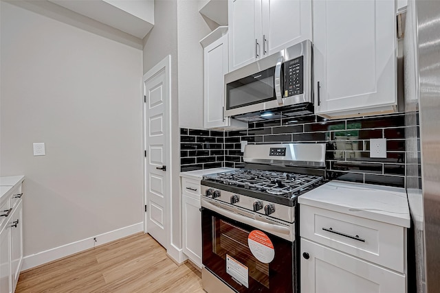 kitchen featuring backsplash, appliances with stainless steel finishes, light hardwood / wood-style floors, light stone counters, and white cabinetry