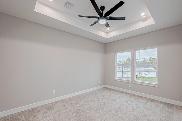 unfurnished room with a tray ceiling, ceiling fan, and light colored carpet