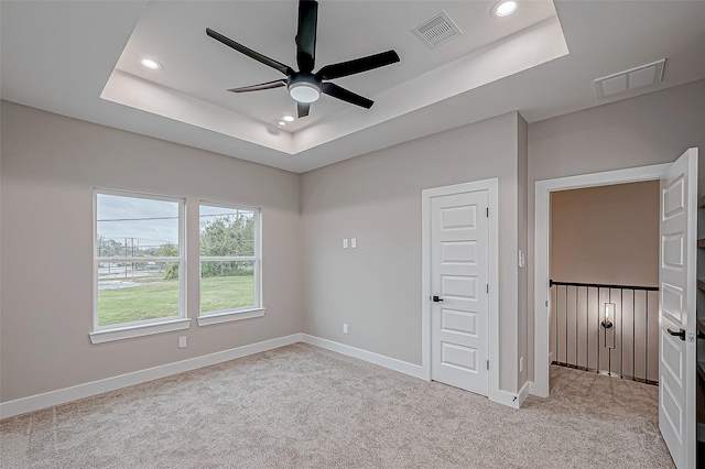 unfurnished bedroom with ceiling fan, light carpet, and a tray ceiling