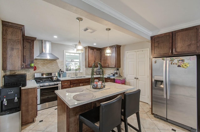 kitchen featuring sink, wall chimney exhaust hood, stainless steel appliances, decorative light fixtures, and a kitchen island