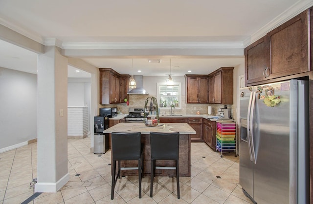 kitchen with hanging light fixtures, stainless steel appliances, wall chimney range hood, a breakfast bar area, and a kitchen island