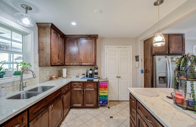 kitchen featuring sink, stainless steel fridge with ice dispenser, light stone counters, backsplash, and decorative light fixtures