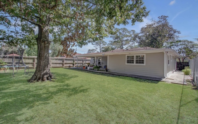 rear view of house with a yard, a trampoline, and a patio