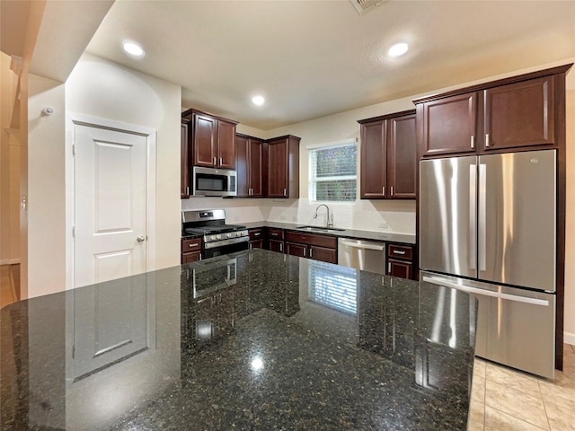 kitchen featuring sink, light tile patterned floors, dark stone counters, and appliances with stainless steel finishes