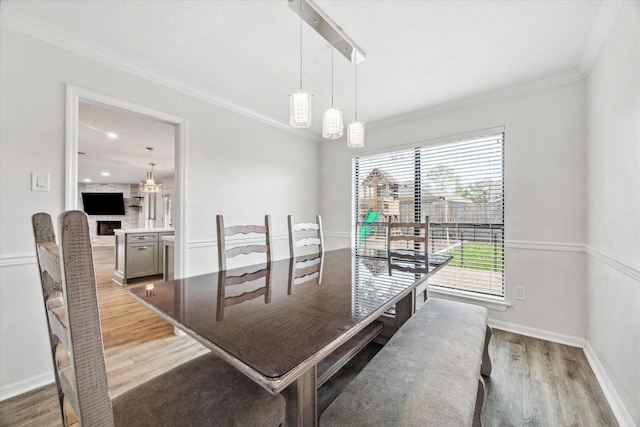 dining area with a fireplace, an inviting chandelier, crown molding, and light hardwood / wood-style flooring