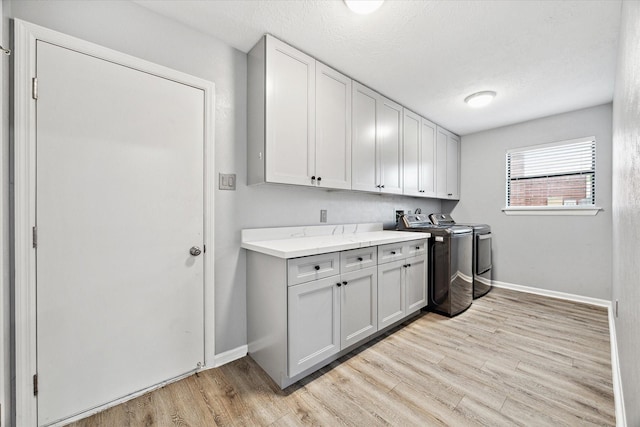 laundry area featuring washing machine and dryer, cabinets, a textured ceiling, and light wood-type flooring