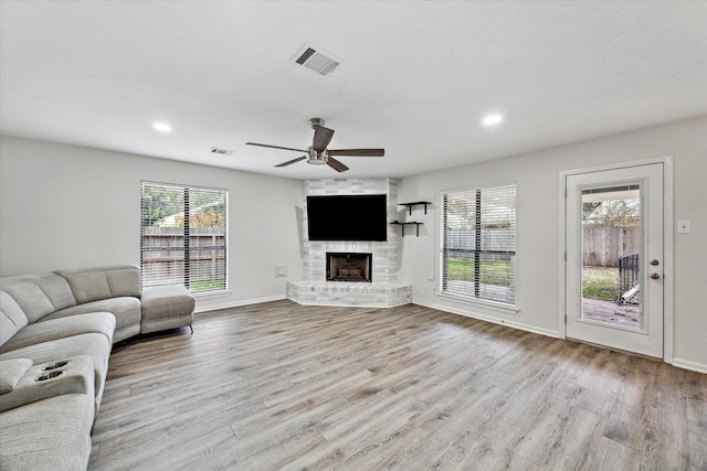 living room featuring a brick fireplace, ceiling fan, plenty of natural light, and light wood-type flooring