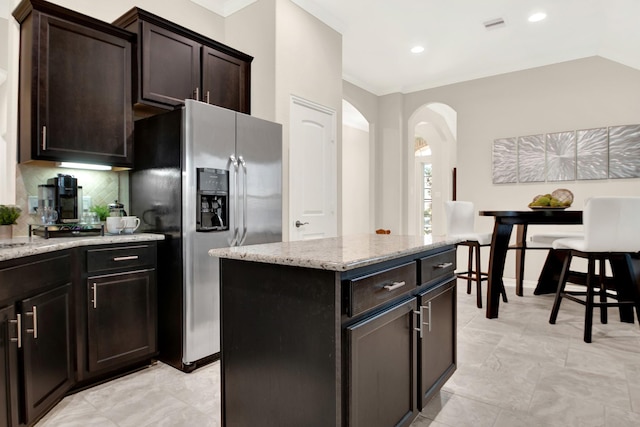 kitchen featuring a center island, vaulted ceiling, decorative backsplash, light stone counters, and stainless steel fridge with ice dispenser