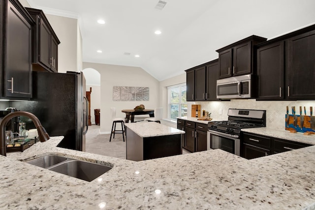 kitchen with lofted ceiling, crown molding, sink, light stone countertops, and stainless steel appliances