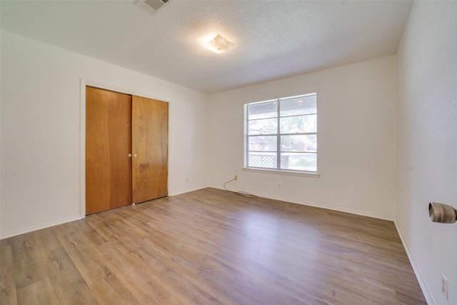 unfurnished bedroom featuring a textured ceiling, light hardwood / wood-style floors, and a closet