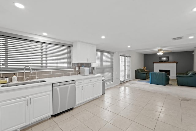 kitchen with sink, a brick fireplace, tasteful backsplash, stainless steel dishwasher, and white cabinets