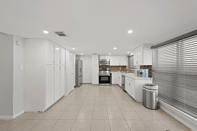 kitchen featuring backsplash, sink, appliances with stainless steel finishes, light tile patterned flooring, and white cabinetry