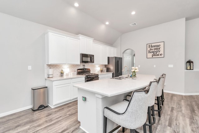 kitchen featuring sink, vaulted ceiling, a kitchen island with sink, white cabinets, and black appliances