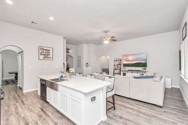 kitchen featuring ceiling fan, a center island with sink, white cabinets, and light wood-type flooring