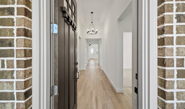 corridor featuring light hardwood / wood-style flooring, brick wall, and an inviting chandelier