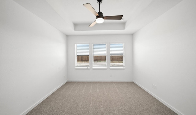 spare room featuring light carpet, a tray ceiling, and ceiling fan