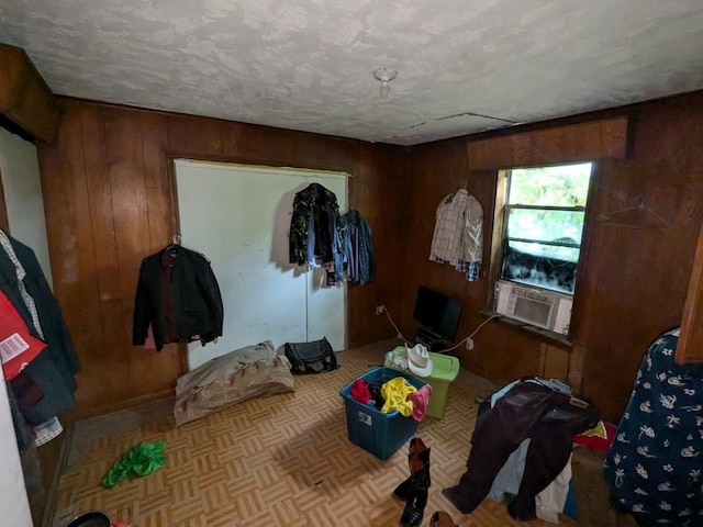 bedroom with a textured ceiling, cooling unit, wooden walls, and light parquet flooring