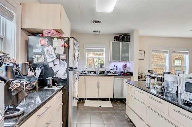 kitchen with sink, dark stone countertops, dark tile patterned floors, a textured ceiling, and stainless steel appliances