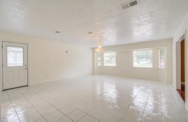 tiled empty room with a textured ceiling and an inviting chandelier