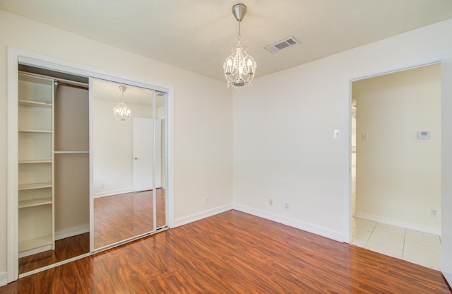 unfurnished bedroom featuring hardwood / wood-style flooring, a closet, and a notable chandelier