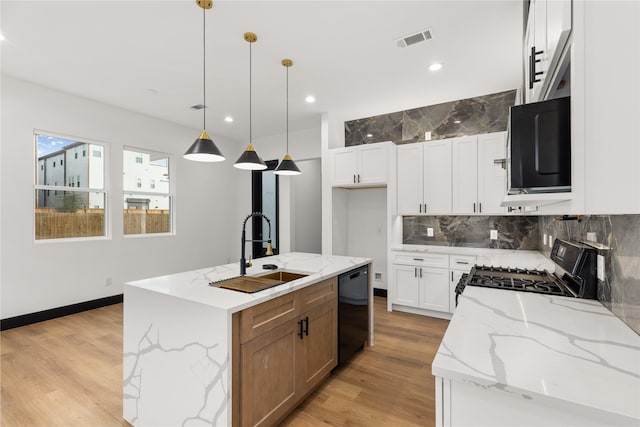 kitchen with white cabinets, sink, light stone countertops, and an island with sink