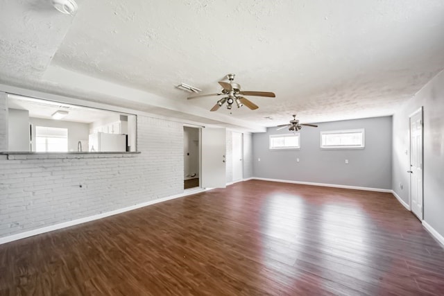 spare room with a textured ceiling, dark hardwood / wood-style flooring, ceiling fan, and brick wall