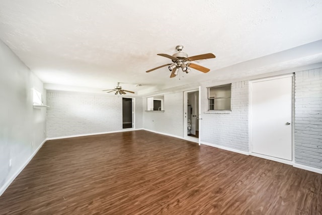 unfurnished living room with a textured ceiling, ceiling fan, dark wood-type flooring, and brick wall