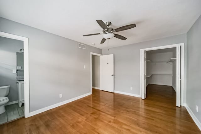 unfurnished bedroom with a walk in closet, ensuite bathroom, ceiling fan, wood-type flooring, and a closet