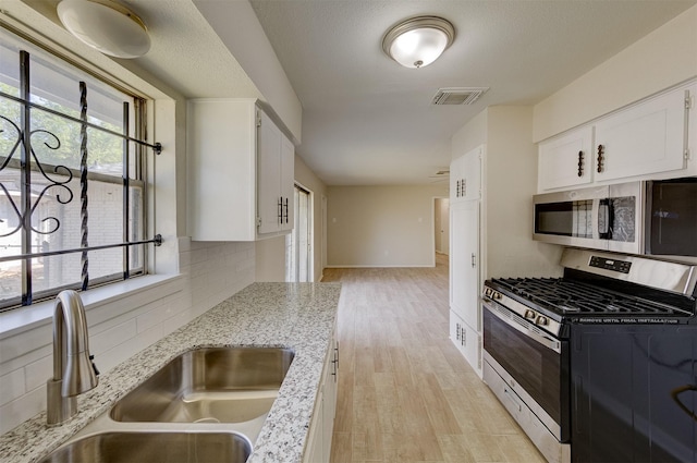 kitchen featuring light stone countertops, sink, light hardwood / wood-style floors, white cabinets, and appliances with stainless steel finishes