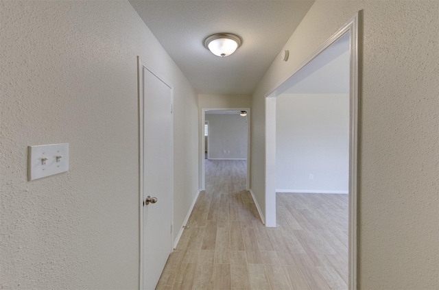 hallway with light hardwood / wood-style floors and a textured ceiling