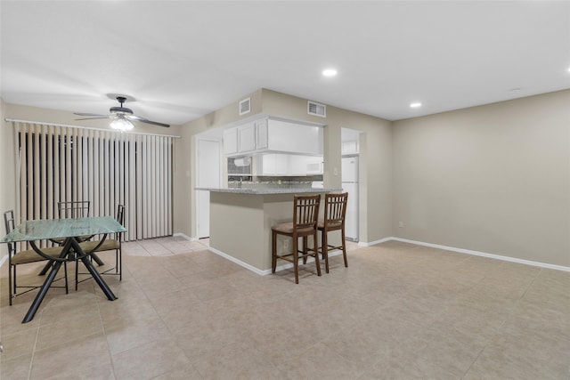 kitchen with white cabinets, ceiling fan, white fridge, a kitchen bar, and kitchen peninsula