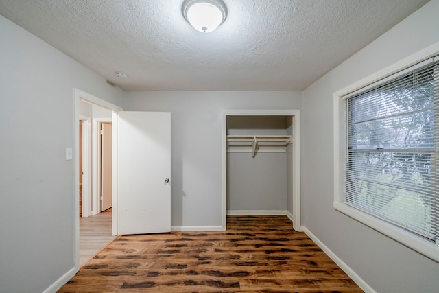 unfurnished bedroom featuring a textured ceiling, a closet, and dark wood-type flooring