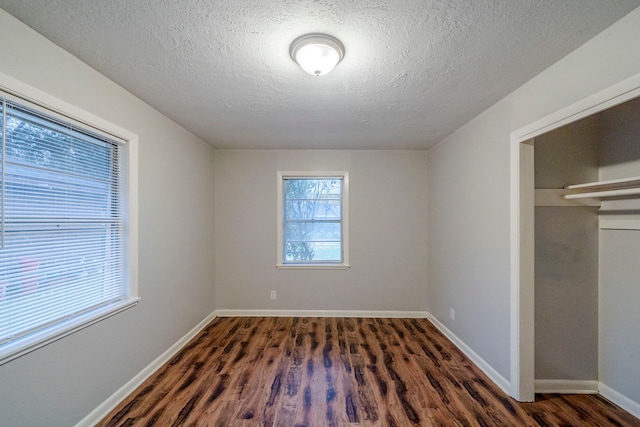 unfurnished bedroom featuring multiple windows, dark hardwood / wood-style flooring, a textured ceiling, and a closet