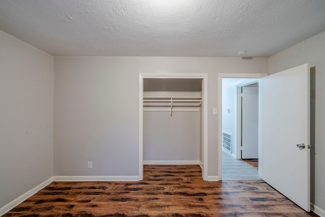 unfurnished bedroom with a textured ceiling, dark hardwood / wood-style flooring, and a closet