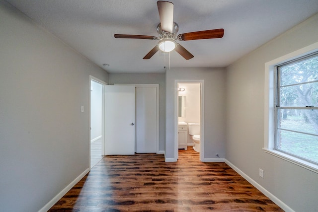 unfurnished bedroom featuring ceiling fan, dark hardwood / wood-style floors, connected bathroom, and multiple windows