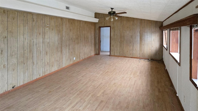 unfurnished room featuring ceiling fan, wood walls, wood-type flooring, and vaulted ceiling