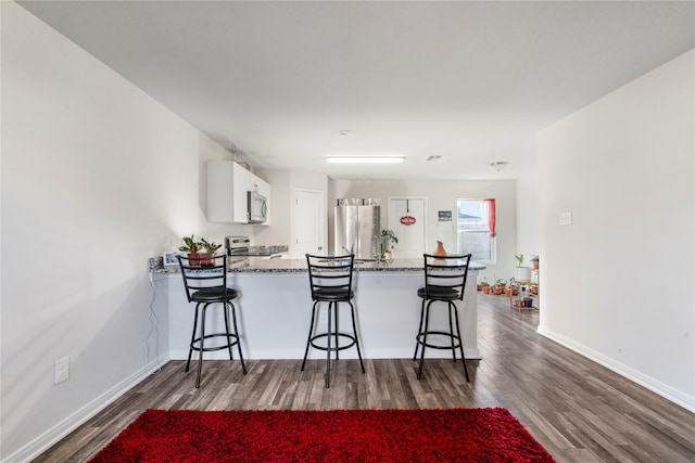 kitchen with kitchen peninsula, a kitchen breakfast bar, stainless steel appliances, white cabinets, and dark hardwood / wood-style floors