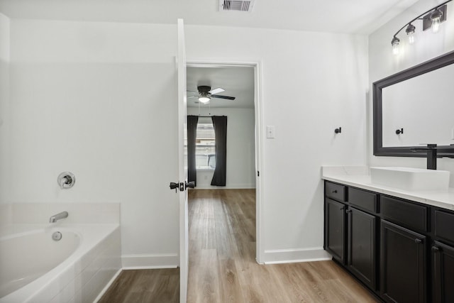 bathroom with hardwood / wood-style floors, ceiling fan, a relaxing tiled tub, and vanity