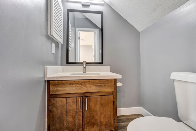 bathroom featuring toilet, a textured ceiling, lofted ceiling, and vanity