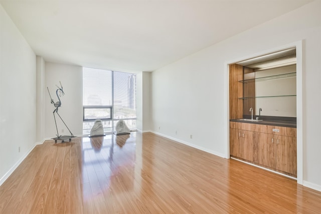 unfurnished living room featuring floor to ceiling windows, light hardwood / wood-style flooring, and sink