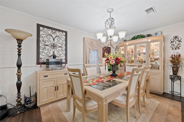 dining room featuring a textured ceiling, crown molding, light hardwood / wood-style floors, and a notable chandelier