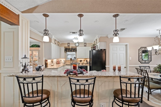 kitchen with kitchen peninsula, light stone countertops, black refrigerator, backsplash, and white cabinetry