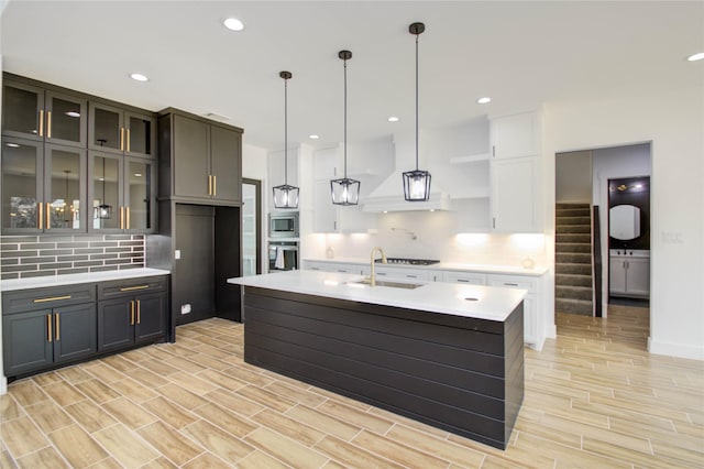 kitchen with an island with sink, appliances with stainless steel finishes, tasteful backsplash, decorative light fixtures, and light hardwood / wood-style floors