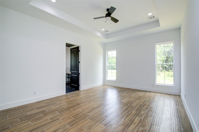 empty room with hardwood / wood-style floors, a tray ceiling, and ceiling fan