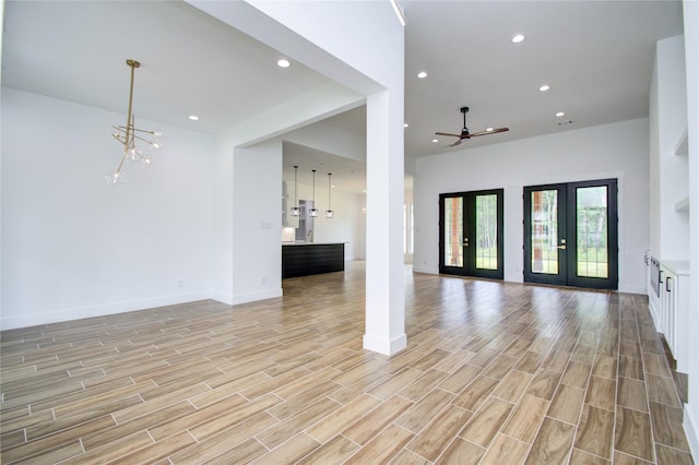 unfurnished living room featuring french doors, ceiling fan with notable chandelier, and light hardwood / wood-style floors